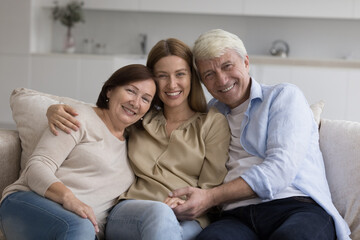 Happy adult daughter woman enjoying meeting with senior parents at home, hugging mature mom and dad...