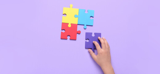 Child's hand with puzzle pieces on lilac background. Concept of autism spectrum disorder