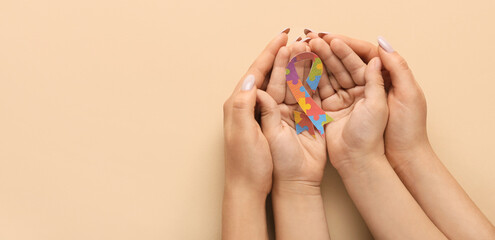 Hands of mother and child holding awareness ribbon on beige background with space for text. Concept...