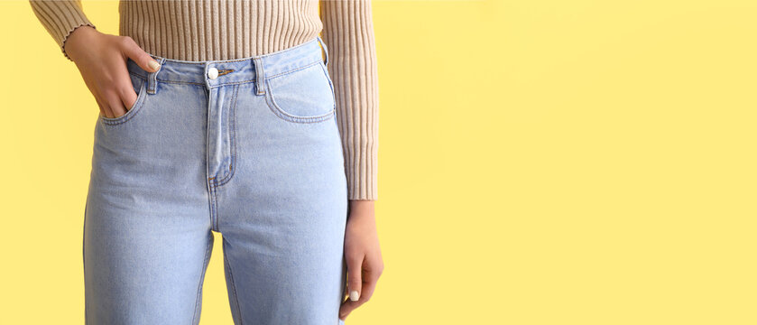 Young woman in stylish jeans on yellow background with space for text