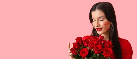 Beautiful young woman with kiss marks on her face and bouquet of red roses on pink background with space for text