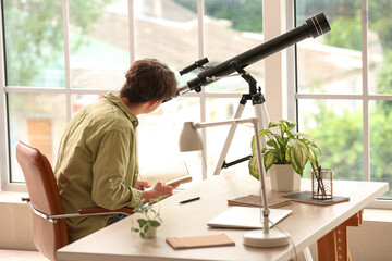 Young male student using telescope at home
