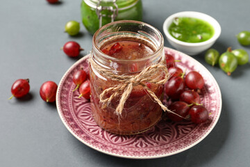 Jar with tasty gooseberry jam on grey background