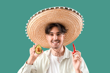 Young Mexican man with chili pepper and avocado on green background