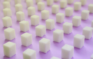 Many small sugar cubes are lined up on a violet background. The concept of diabetes and excess...