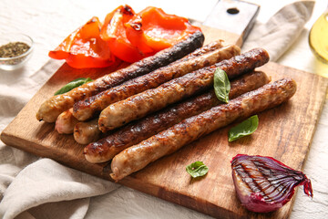 Wooden board of tasty grilled sausages and vegetables on white background