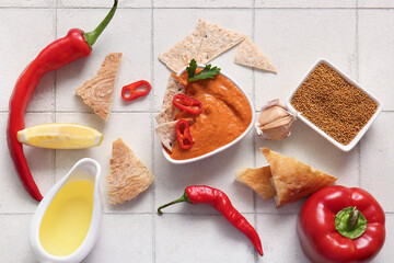 Bowl of tasty muhammara and ingredients on white tile background