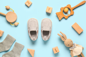 Stylish baby shoes with socks and different toys on blue background