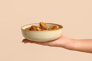 Female hand holding bowl with tasty dried figs on beige background