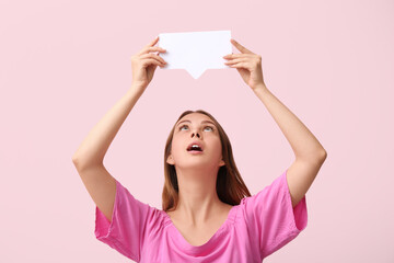Surprised young woman holding blank speech bubble on pink background