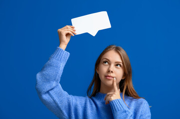 Thoughtful young woman holding blank speech bubble on blue background