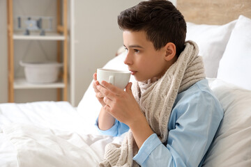 Sick little boy drinking tea in bedroom