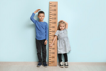 Cute little children measuring height near blue wall