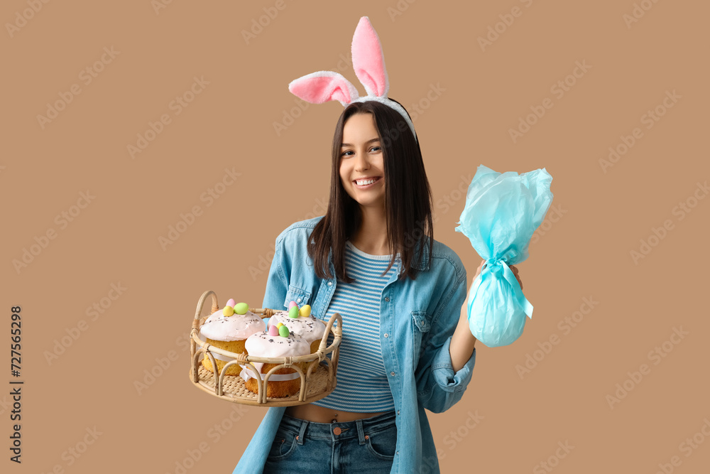 Poster pretty young woman with bunny ears, easter basket and gift on beige background