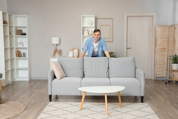 Young man behind grey sofa in living room