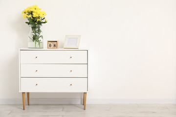 Vase with yellow flowers, calendar and photo frame on dresser near white wall. International Women's Day celebration