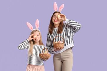 Cute little girl and her mother in bunny ears holding baskets with painted Easter eggs on lilac...
