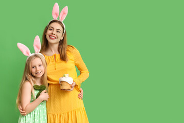 Cute little girl with rabbit and her mother in bunny ears holding Easter cake on green background