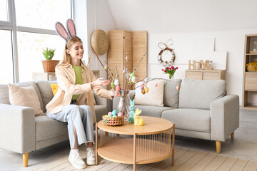Young woman in bunny ears with willow branches and Easter eggs at home