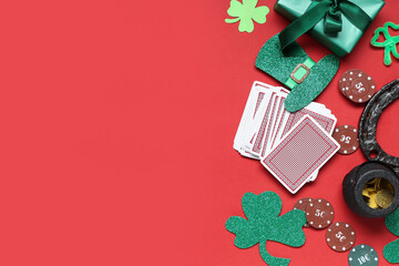 Poker chips, cards, gift box and decorations for St. Patrick's Day celebration on red background