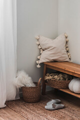 A cozy home interior - an oak bench with a decorative pillow, a carpet, a plaid in a basket in the...