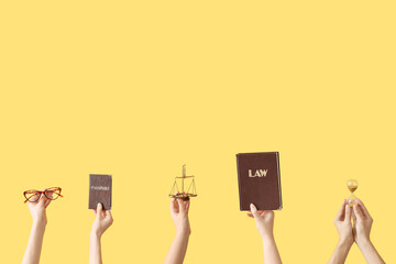 Female hands holding hourglass, scales of justice, law book and passport on yellow background