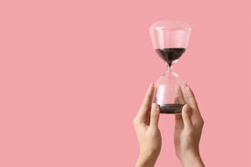 Female hands holding hourglass on pink background