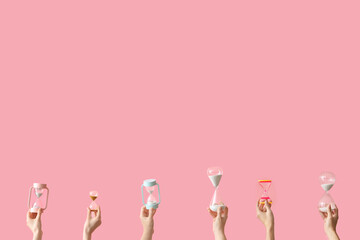 Female hands holding hourglasses on pink background