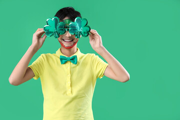 Funny boy with face painting and clover shaped novelty glasses on green background. St. Patrick's...
