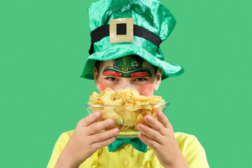 Funny boy with face painting, leprechaun's hat and potato chips on green background. St. Patrick's...