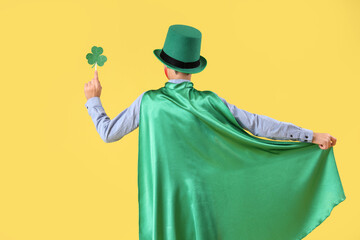 Funny boy with green cape, clover and leprechaun's hat on yellow background, back view. St....