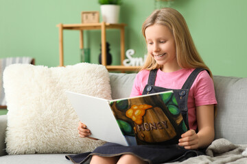 Little girl reading book while sitting on sofa at home