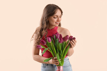 Pretty young woman with bouquet of beautiful purple tulips on beige background