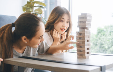 Two asian woman lifestyle playing wooden block tower board game at home apartment