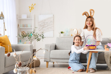 Cute little girl with Easter basket and her mother in bunny ears at home