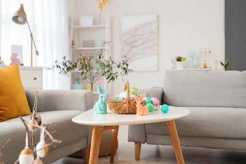 Wicker basket with Easter cake, eggs and toy rabbits on table in living room