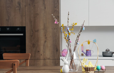 Vase with willow branches and Easter eggs on table in kitchen