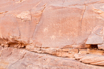 Ancient drawings of the animals and the life scenes carved into stone on the rock wall in the endless sandy red desert of the Wadi Rum near Amman in Jordan