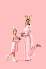 Cute little girl and her mother in bunny ears with Easter eggs on pink background