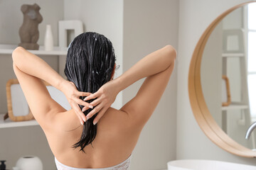 Young woman applying hair mask in bathroom, back view