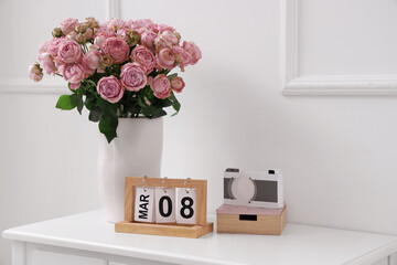 Calendar with date of International Women's Day and roses in vase on table near light wall - Powered by Adobe