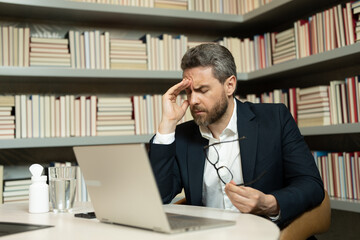 Sad man got migraine touches her head because of pain. Man manager with strong headache working on laptop. Overworked freelancer or manager at office. Stressed, tired man with headache.