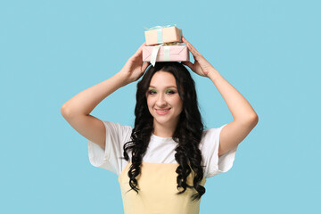 Beautiful young woman with gift boxes on blue background. International Women's Day