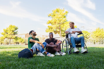 Young Black man in a wheelchair and friends laughing and having fun sitting on the grass in a park....