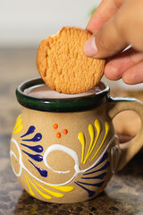 person dipping cookie into hot chocolate drink in traditional Mexican mug