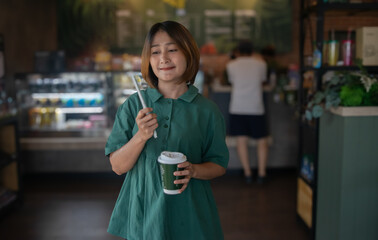 Woman standing in the cafe holding a drink with a paper straw and coffee cup,smiling and looking at the camera,relaxing on holiday,lifestyle concepts.