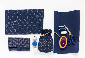 Materials for embroidery in Sashiko style with white threads on blue fabric and hand embroidered handbags on white work table. Embroidery and sewing as a hobby. Handmade gifts