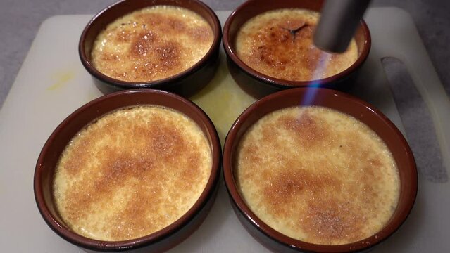 A cook applies a hot torch to the sugar surface of a creme brulee dessert to caramelize the top.  