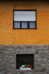 Fototapeta na wymiar Yellow and stone wall of a traditional house and wooden window with white wooden shutters in Szentendre, Hungary