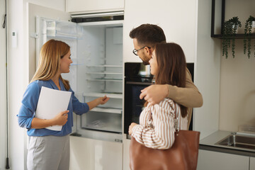 Female shop assistant helping young couple choose new refrigerator